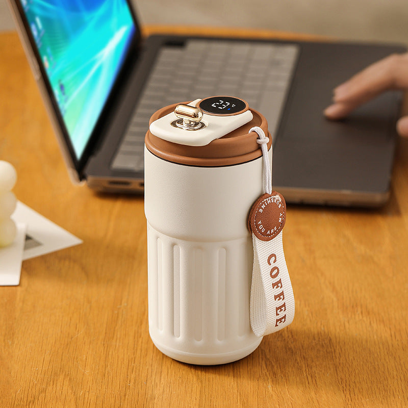 Insulated beige tumbler with digital temperature display, brown lid, and "COFFEE" ribbon tag.