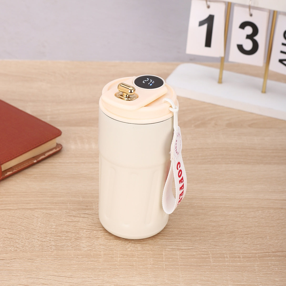 A stainless steel thermos with a digital temperature display on a wooden table next to a notepad and a calendar.