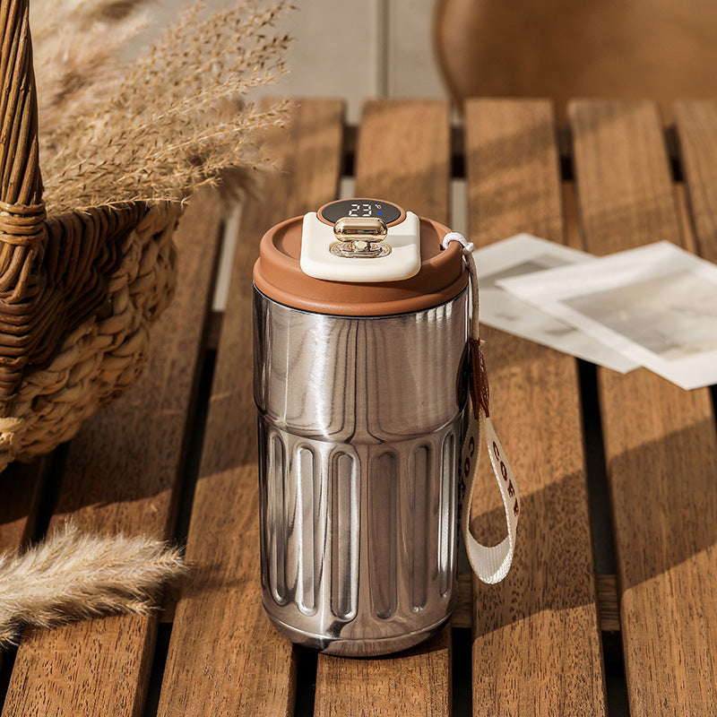Stainless steel thermos with brown and cream lid and temperature display on a wooden table.
