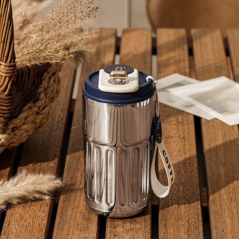 Stainless steel tumbler with a temperature display and a woven strap.