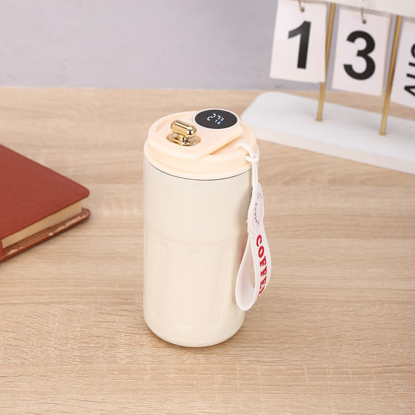 A stainless steel thermos with a digital temperature display on a wooden table next to a notepad and a calendar.
